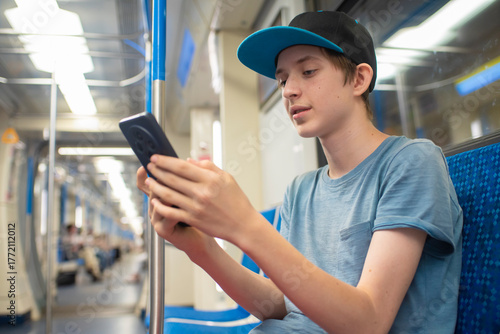 Fotografie A teenage boy in a cap holds a phone, surfs the Internet, sits on a subway train