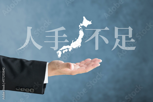 日本列島の地図と人手不足の文字を掲げるスーツを着た人物の手