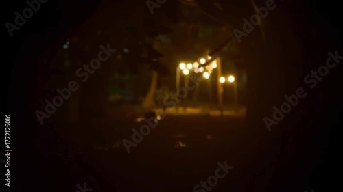 Blurry nighttime scene through a peephole of a lit patio area surrounded by trees