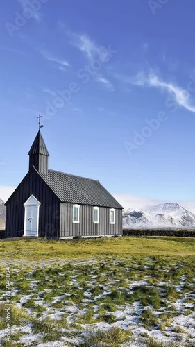 The famous black church Búðakirkja on the Snæfellsnes Peninsula, Iceland, surrounded by lava fields, green moss and snowy mountain views, is a landmark and a popular tourist destination.