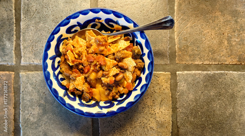 bowl of homemade chile con carne with cheddar cheese and corn chips