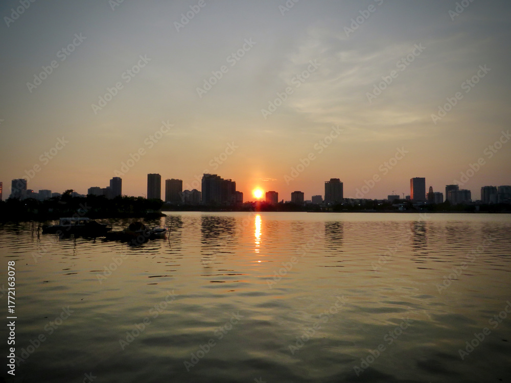Naklejka premium Symmetry at Sunset: City Skyline Reflected on Still Water on West Lake in Hanoi, Vietnam