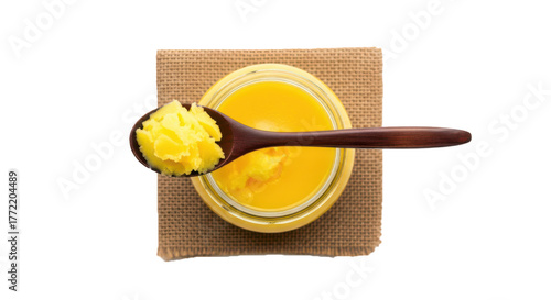 Wooden spoon with fresh yellow ghee in glass jar on rustic mat top view