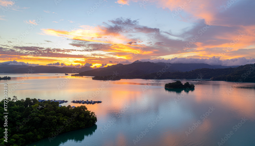 Fototapeta premium A breathtaking aerial view of a calm tropical lake dotted with small islands at sunrise. The vibrant orange and pink clouds beautifully reflect on the water surface.