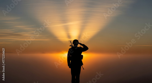 Silhouette of a soldier saluting during sunset or sunrise with sun rays.