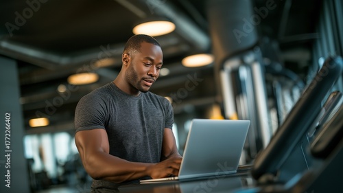 A young, attractive man working as a fitness teacher in a gym is using a laptop.
