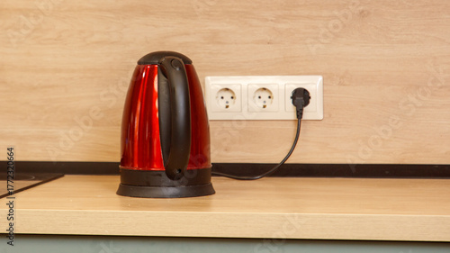 A red electric kettle sits on a wooden counter next to a power outlet