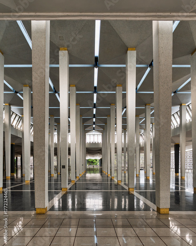 Masjid Negara, aka National Mosque interior, Kuala Lumpur, Malaysia. Modern architectural design with repeating tiled columns, golden bases, reflective floors, and geometric skylit ceiling.