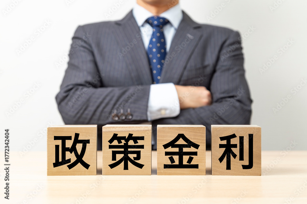 Obraz premium 「政策金利」と書かれたブロックと腕組みをするビジネスマン