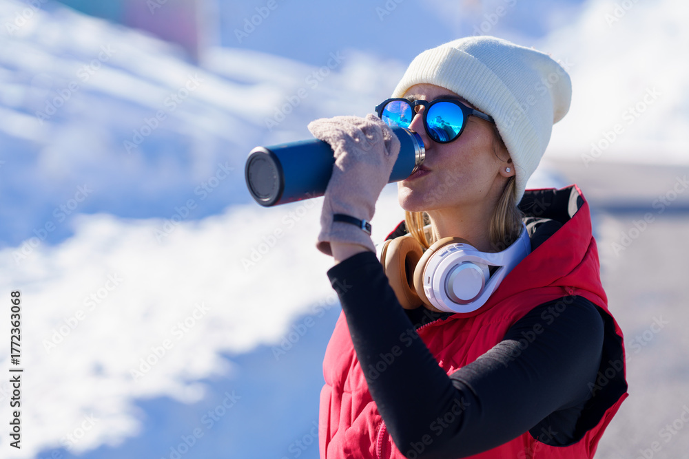 Obraz premium Athletic woman in warm clothes drinking water in nature