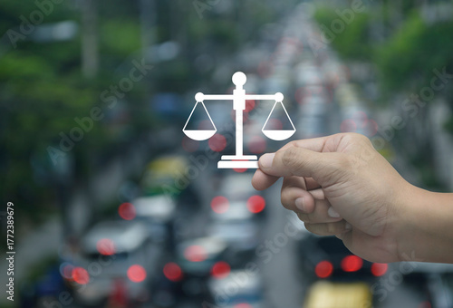 Hand holding law flat icon in fingers over blur of rush hour with cars and road in city, Business legal service concept