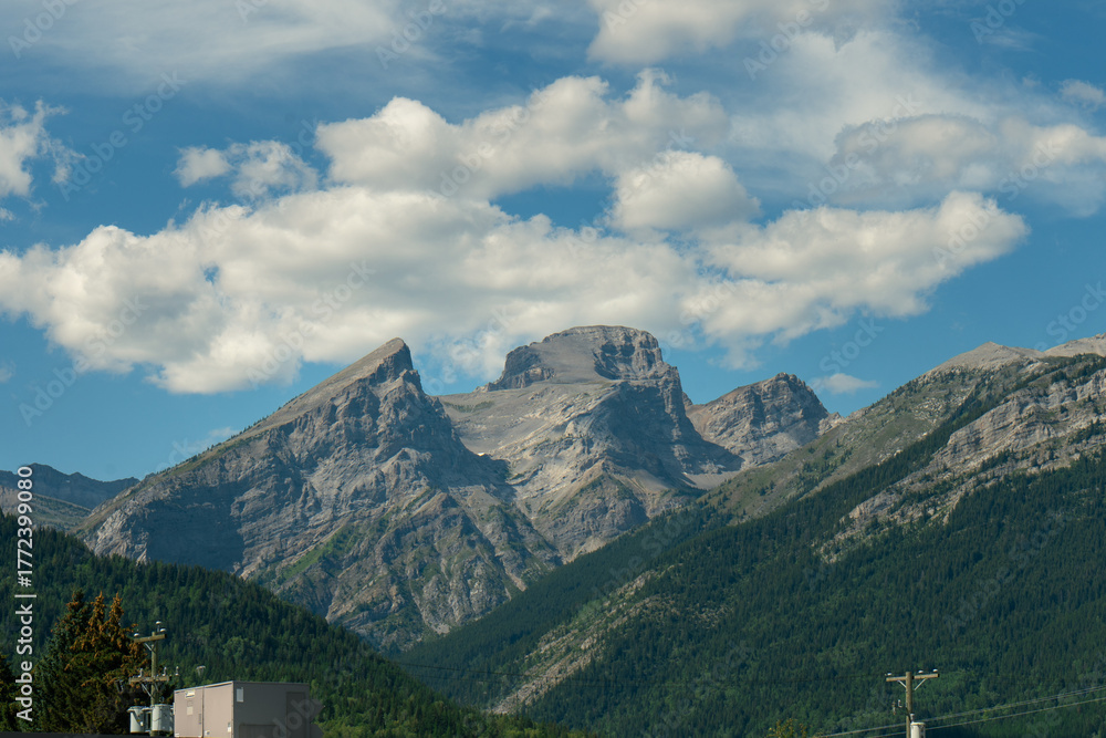 Obraz premium Majestic rocky mountains against a vibrant blue sky dotted with white clouds.