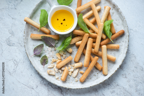 Breadsticks served with salt, olive oil and basil leaves on a grey plate, horizontal shot, middle closeup