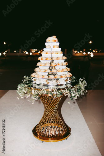 The bride's cake, gold stand decorated with flowers. There are white chocolate chip cookies on every shelf. The cakes are decorated with gold leaf.