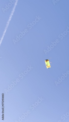A parachutist flying in a parachute against a blue sky. A parachute jump, seen from the ground. Gliding under a parachute canopy