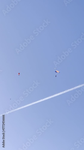 A parachutist flying in a parachute against a blue sky. A parachute jump, seen from the ground. Gliding under a parachute canopy