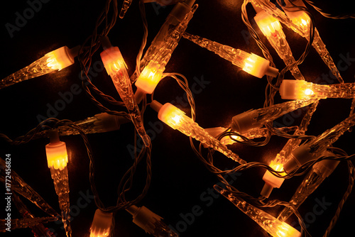 Guirlande lumineuse de Noël vintage avec ampoules en forme de glaçons stalactites, posée en vrac sur fond brun foncé, vue zénithale, lumière orangée dans la nuit