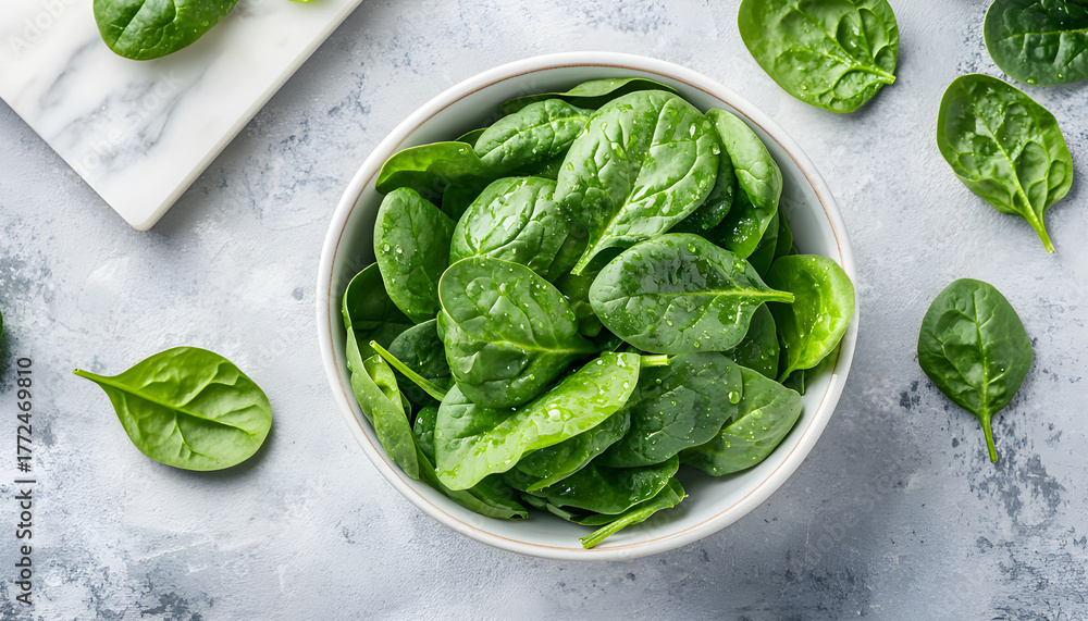 Obraz premium Fresh spinach leaves on white plate. Healthy vegan food. Top view