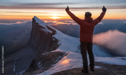 Person celebrates peak achievement with raised arms as the sun sets over snowy mountain range