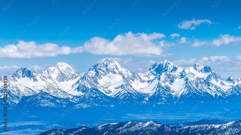 Obraz premium Panoramic view of majestic snow-capped mountains under vibrant blue sky adorned with fluffy white clouds, showcasing breathtaking winter alpine landscape