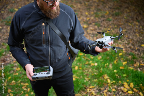 A person stands in a lush green area, holding a drone while gripping a controller. The sunlight filters through trees, creating a serene atmosphere for exploration.