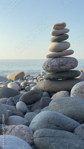 Balanced stack of smooth stones on a pebble beach with ocean waves and sailboat in the background under a clear sky at sunset
