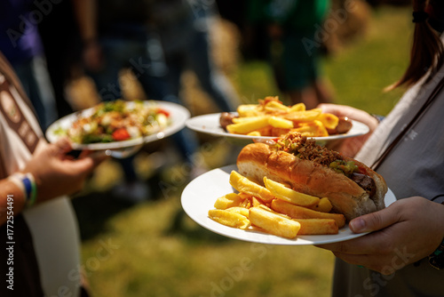 People carrying plates with fries and sandwiches