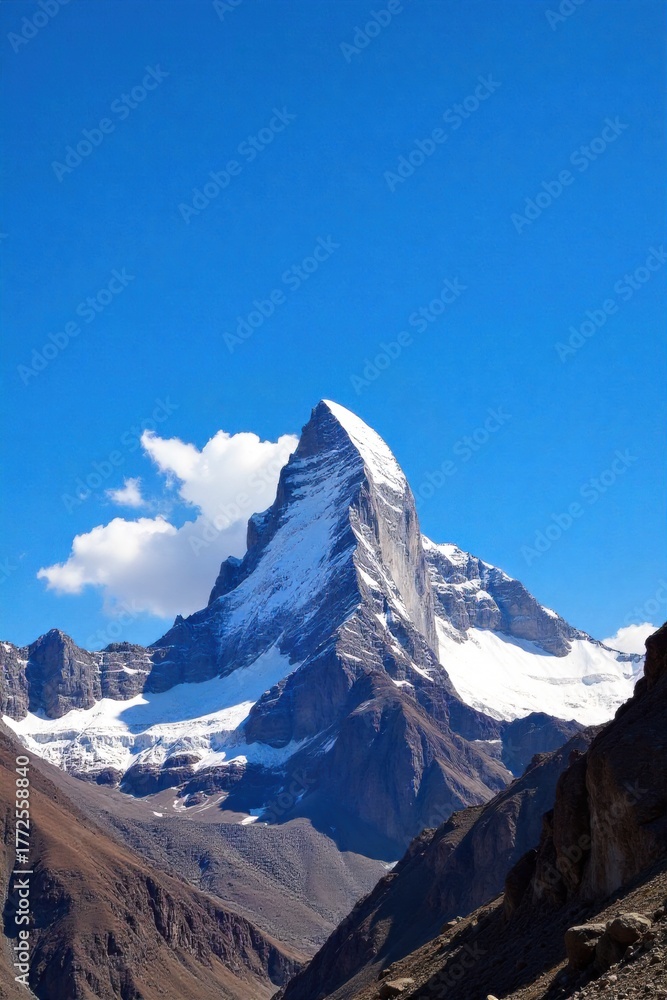 Fototapeta premium Snow Capped Mountain Peak Landmark in Daylight A majestic snow capped mountain peak under a clear, bright blue daylight sky. The surrounding landscape is rugged and natural, with hints of rocky
