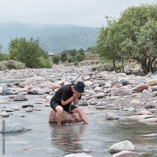 Man washing his face in clear mountain river on hot summer day