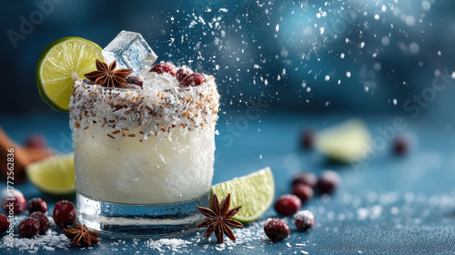 A glass of margarita with a lime wedge and a sprinkle of cinnamon on top. The drink is served on a blue table with a few cranberries scattered around it