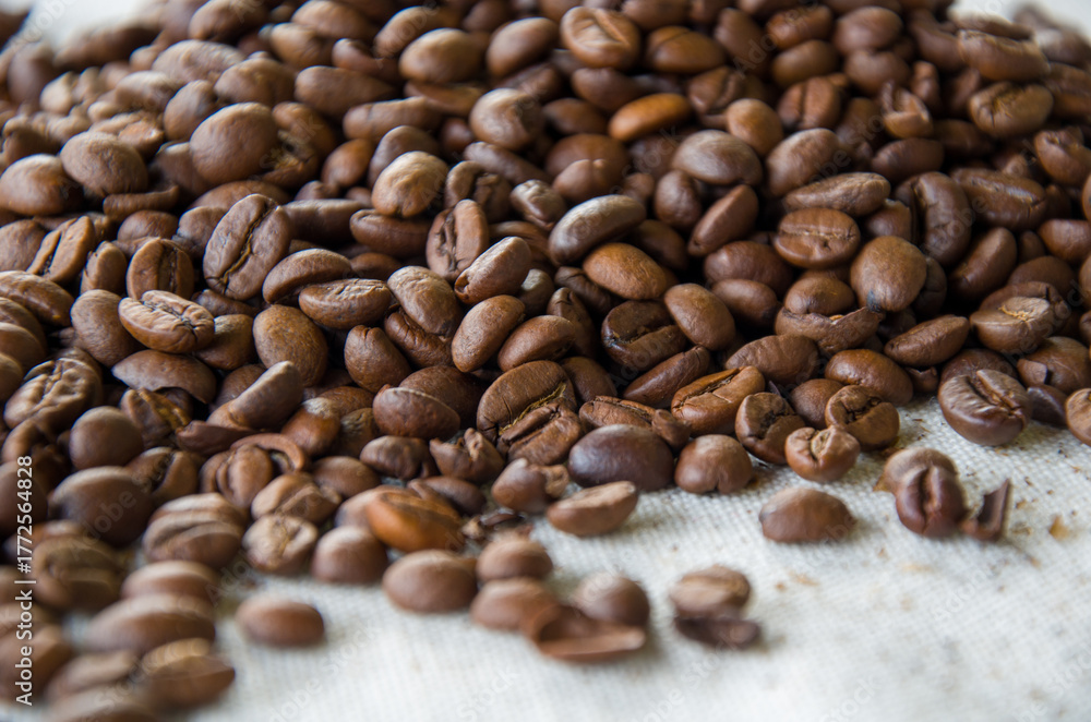 Fototapeta premium A close-up shot of a large pile of freshly roasted brown coffee beans on a textured white fabric.