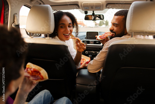Photos Excited Latin family, parents and boy sitting in car and eating pizza during the