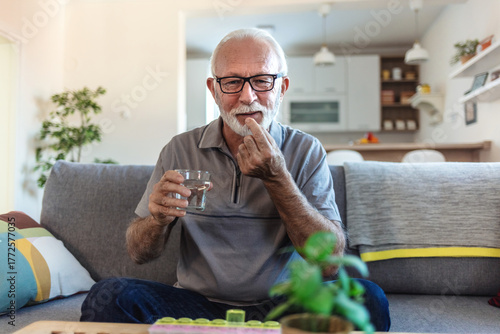Fotografie Senior man takes pill with glass of water in hand