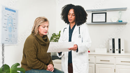 Doctor Discussing Patient Medical Report With Older Woman In Clinic Office Setting During Consultation Today