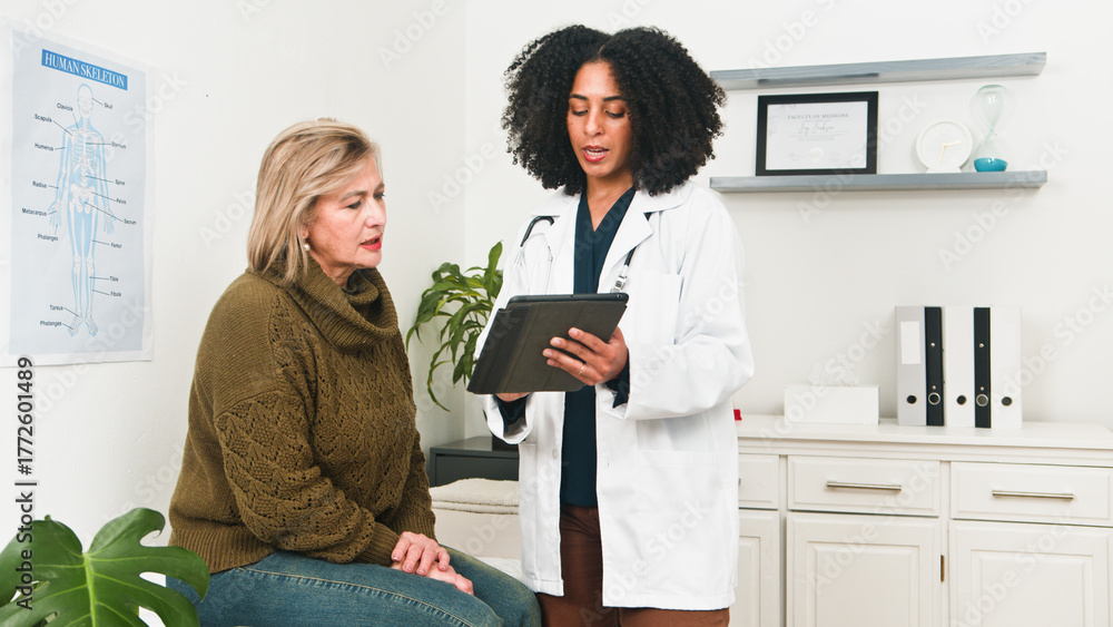 Fototapeta premium Compassionate Doctor Counsels Patient In Clinic While Using Tablet For Medical Advice