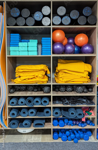 Yoga props and pilates equipment, studio with mats, dumbbells, rollers, and blocks on wooden shelves. Minimalist gym interior, clean and organized space.