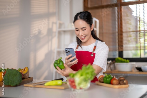 Принти на полотні Woman cooking, following online healthy vegetable recipe on smartphone
