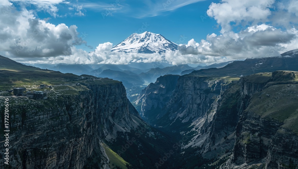 Naklejka premium Aerial perspective over a lush green valley leading to a steep gorge with jagged cliffs set against towering snow-capped mountains, showcasing erosion risk