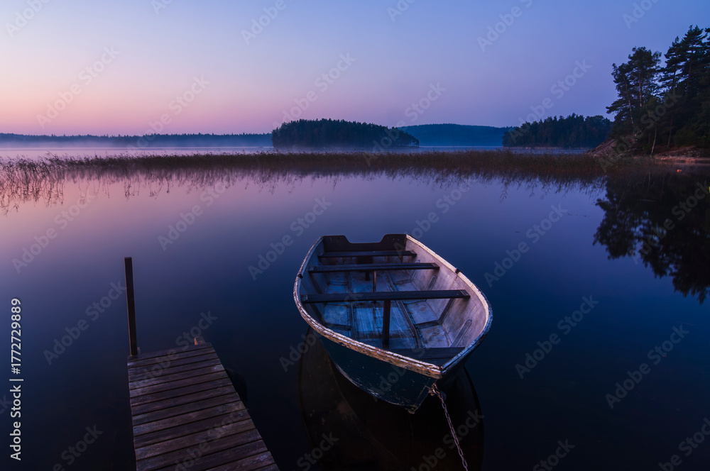 Obraz premium Still boat on a calm lake at sunrise near Gothenburg in Sweden with soft colors reflecting on the water