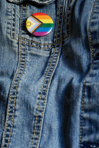 Close-up of an LGBTQ+ pride button pinned to a blue denim jacket. The badge features the inclusive Pride flag colors, symbolizing support, equality, and identity expression within the LGBTQ+ community