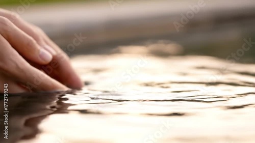 Soft human hands make contact with the reflective surface of tranquil water.