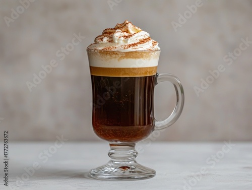 Irish coffee in a clear glass mug with whipped cream and dusting on a plain surface