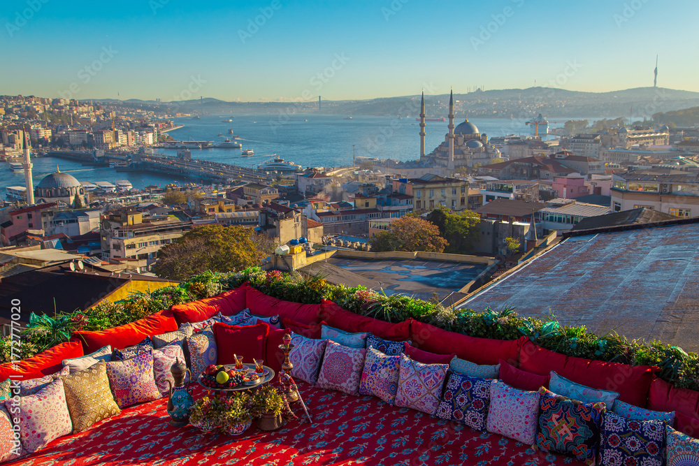 Obraz premium Magnificent panoramic views of Istanbul from the rooftop with a traditional Turkish carpet, pillows, hookah and a fruit table.