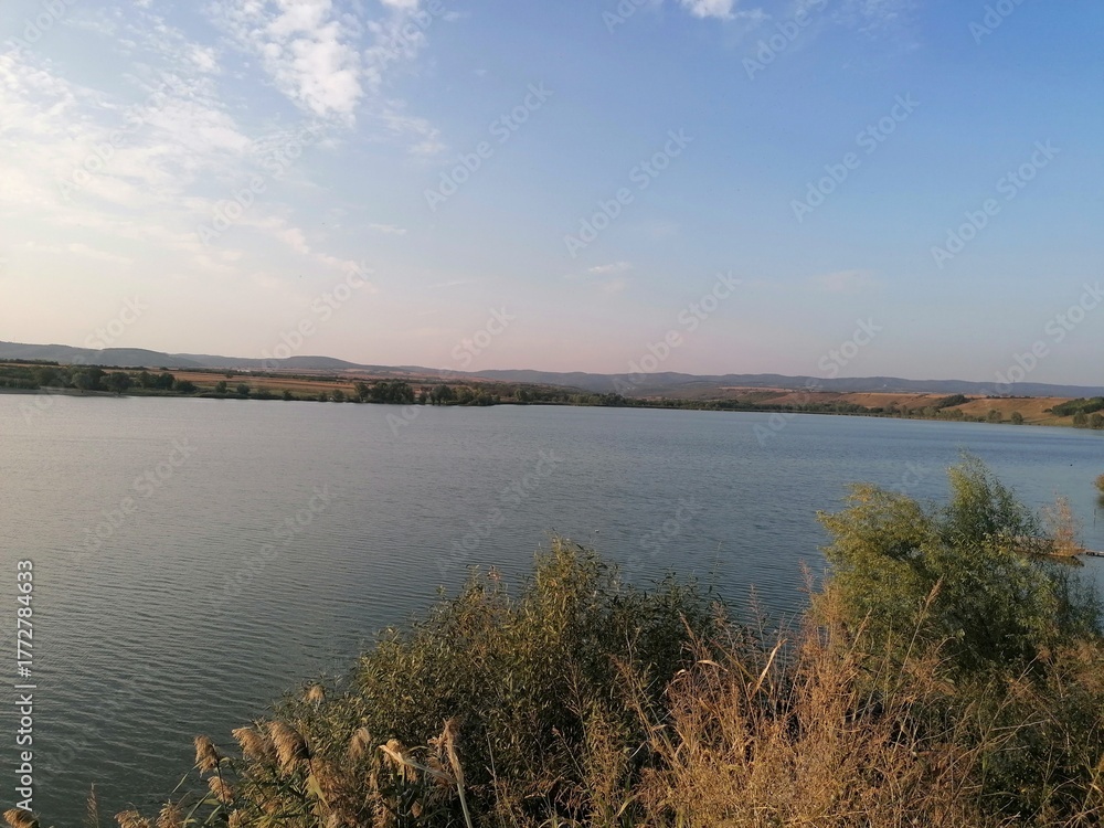 Fototapeta premium Serene Lake and Rolling Hills Landscape at Golden Hour Sunset