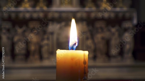 Close-up shot of a lit candle with a blurred background of religious statues.