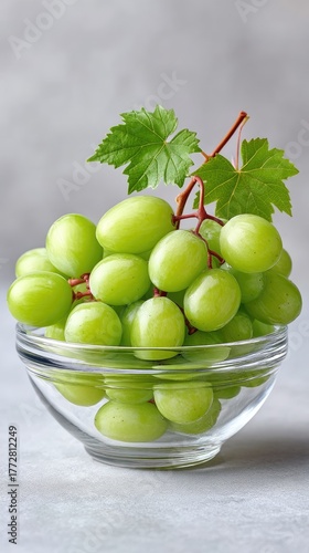 Fresh Green Grapes in a Clear Glass Bowl with Water Droplets and Green Leaves on a Textured Gray Background Studio Shot