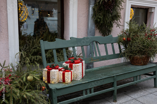 Decorative metal bench in front of a large Christmas tree decorated with red ornaments and garlands. Mnesto for relaxation.