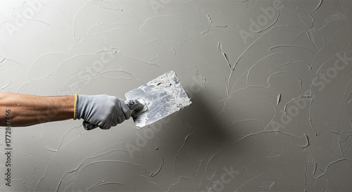 Hand applying textured plaster to a wall, creating a decorative and tactile surface with smooth and curved patterns using a trowel.