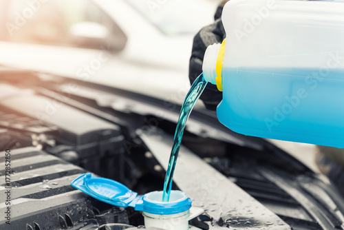 Bild auf Leinwand Close-up detail of driver or mechanic hand in gloves pouring blue antifreeze liquid for winter car windshield screen washing with bootle watering can
