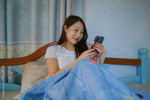 Obraz na plátně A woman is sitting on a bed and looking at her cell phone